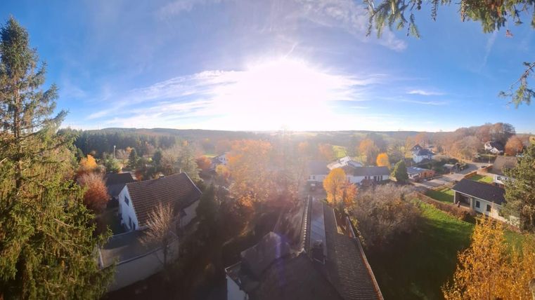 Un paysage pittoresque avec des maisons et des arbres d'automne colorés. Le ciel est clair et le soleil brille intensément.