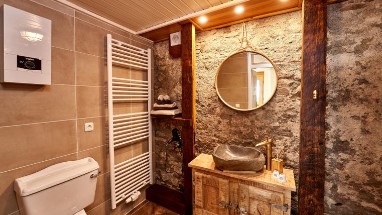 Ein modernes Badezimmer mit einem Holzbecken und einem runden Spiegel. Die Wände sind teilweise mit Stein und Holz dekoriert.