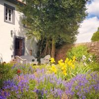 A beautiful garden in front of a house with colorful flowers and a cozy seating area. In the background, there are trees and a clear sky.