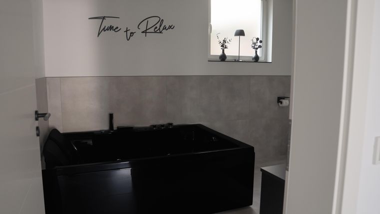 Een moderne badkamer met een zwart bad. Op de muur staat de tekst „Time to Relax“.