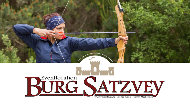 Eine Frau mit einem Pfeil und Bogen zielt auf ein Ziel. Im Hintergrund sind grüne Bäume zu sehen.