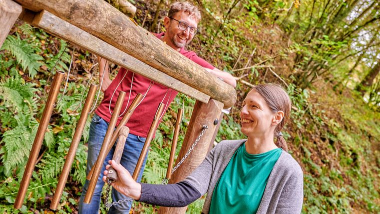 Two people at a wooden chime in the forest.