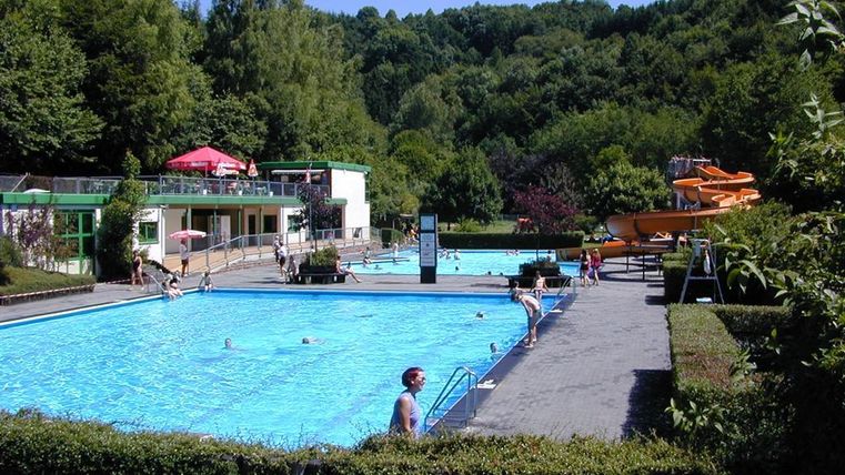 Ein schöner Schwimmbereich mit zwei Pools und einer Rutsche. Die Umgebung ist grün und einladend.