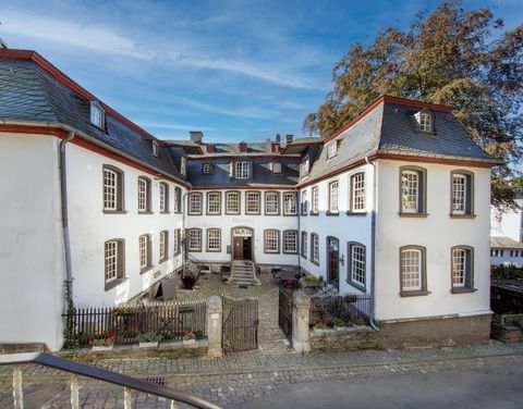 A historic building with a white facade and red accents. In front of the building is a small courtyard with plants.