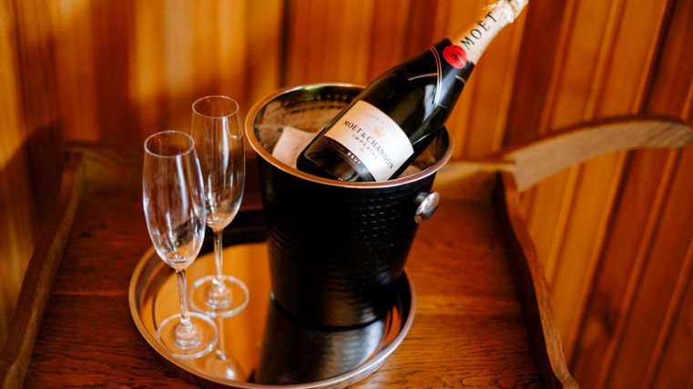 A champagne bottle in an ice bucket is sitting on a tray. Next to it are two champagne glasses.
