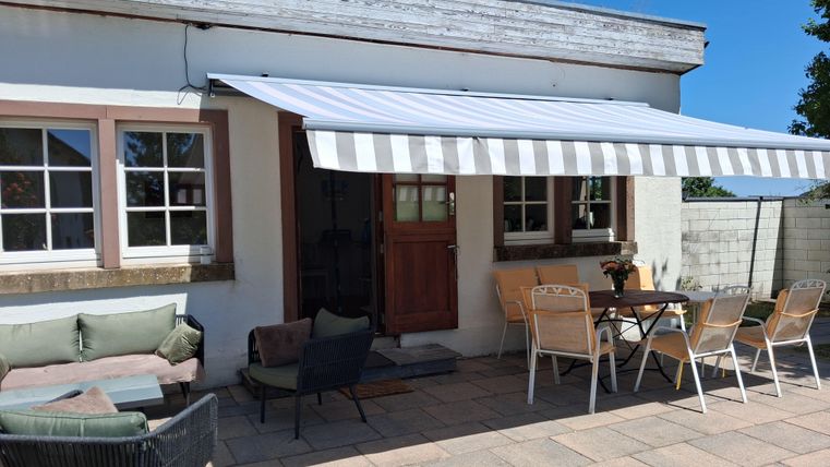 Une terrasse confortable avec un auvent et différents sièges. La zone est claire et accueillante, idéale pour se détendre à l'extérieur.