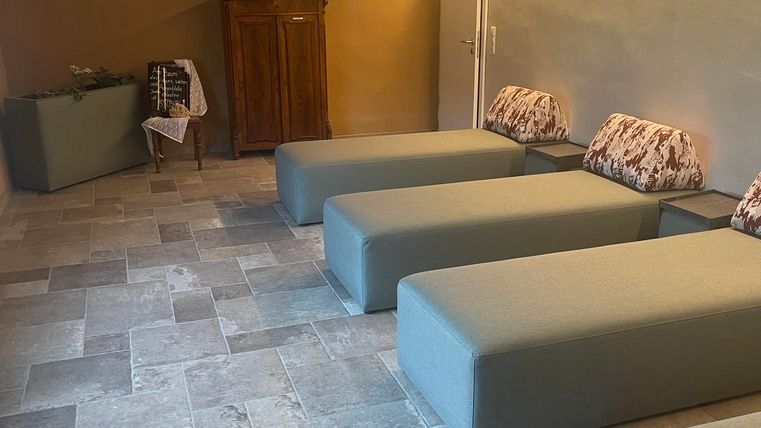 Une salle de détente moderne avec des chaises longues élégantes et un éclairage doux. Le sol est en carrelage gris, et une commode en bois est contre le mur.