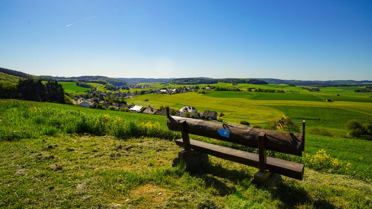 Bench on a hill with far-reaching views over fields, a village and blue sky