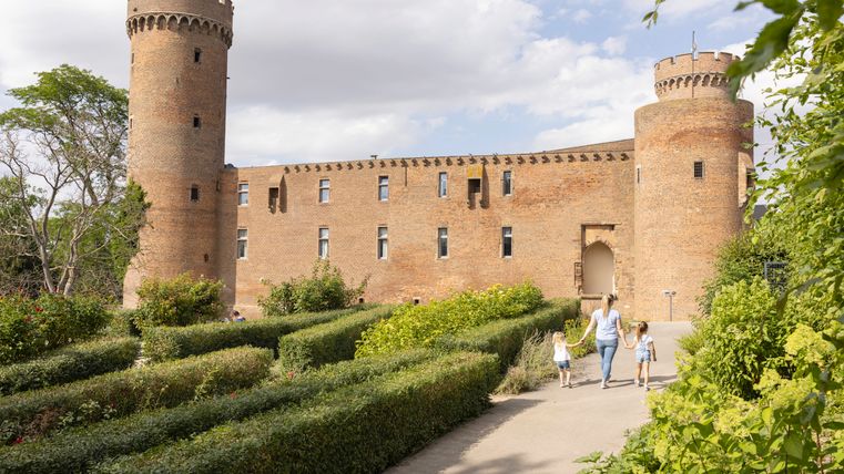 Un château historique avec deux tours rondes et une famille qui se promène dans un jardin bien entretenu.