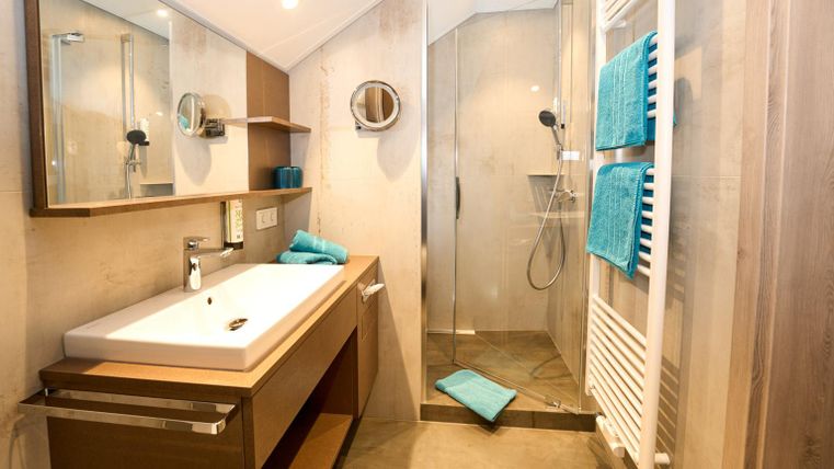 Een moderne badkamer met een douche en een dubbele wastafel. De muren zijn in neutrale tinten gehouden, aangevuld met handdoeken in turquoise.