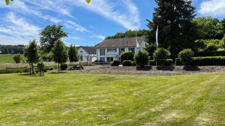Een mooi eigendom met een grote, groene tuin. Op de achtergrond ziet men een modern huis omringd door bomen en struiken.