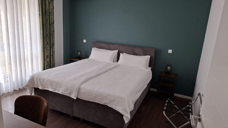 Ein modernes Schlafzimmer mit zwei Einzelbetten und einem minimalistischen Design. Die Wände sind in einem beruhigenden Grünton gestrichen und große Fenster lassen viel Tageslicht herein.