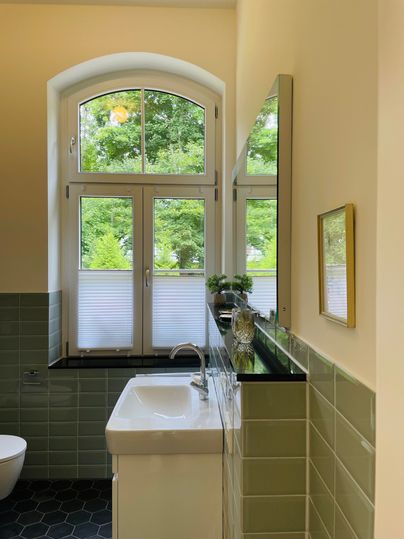 Une salle de bain moderne avec un lavabo et une grande fenêtre. La pièce est claire et accueillante avec des carreaux verts et une vue sur l'extérieur.