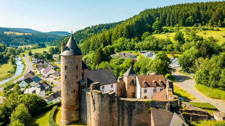 Vue aérienne du château de Bertrada à Mürlenbach, entouré d'un paysage verdoyant et d'une rivière.