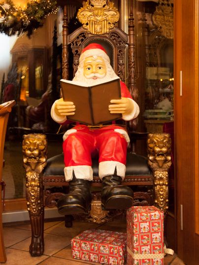 Een feestelijke kerstman zit op een prachtige stoel en leest een boek. Onder hem liggen feestelijk ingepakte cadeaus.