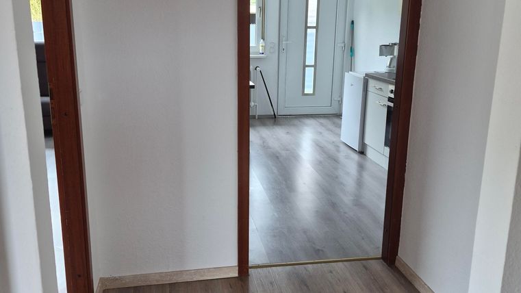 Een heldere gang met houten vloer en twee deuren. Op de achtergrond is een moderne keuken zichtbaar.