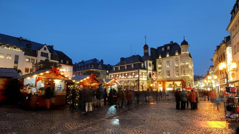 Een feestelijke marktplaats bij schemering met feestelijk versierde stands. Mensen slenteren door de pittoreske omgeving.