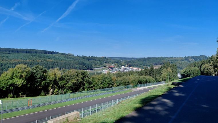 Un aperçu pittoresque d'un paysage verdoyant sous un ciel bleu clair. Au premier plan, une route est visible, traversant la nature.