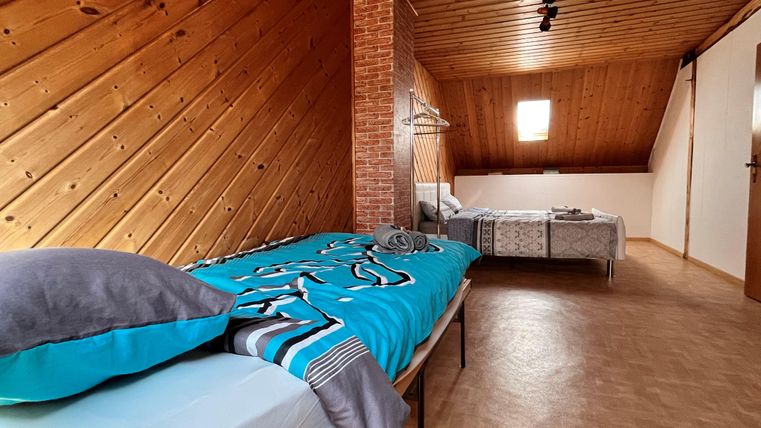 A cozy bedroom in the attic with wooden ceilings and two beds. The room is bright and inviting with a window that lets in light.