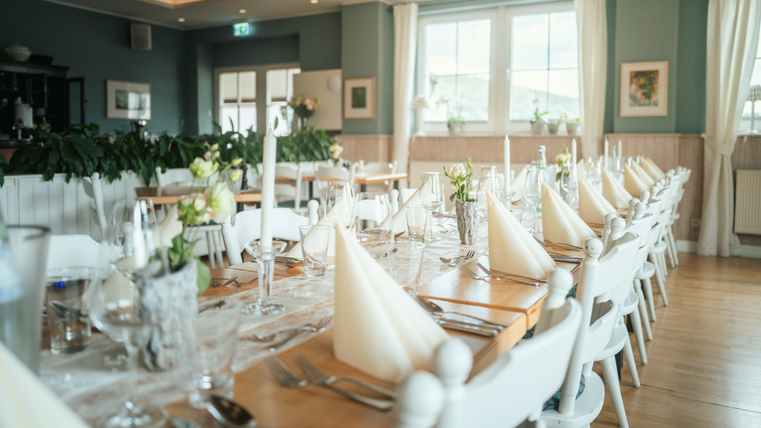 Een elegant gedekte tafel in een lichte restaurant met mooie bloemen en kaarsen. De sfeer voelt uitnodigend en smaakvol aan.