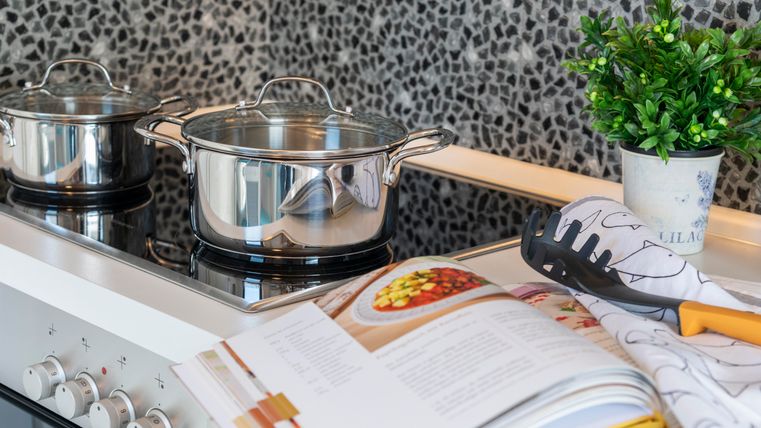 Een moderne keuken met twee pannen op het fornuis. Een kookboek en een klein plantje zijn ook zichtbaar.