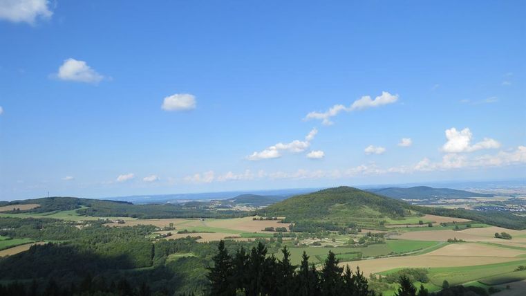 A vast landscape of hills and fields under a clear blue sky. A few clouds are visible, adding to the view.