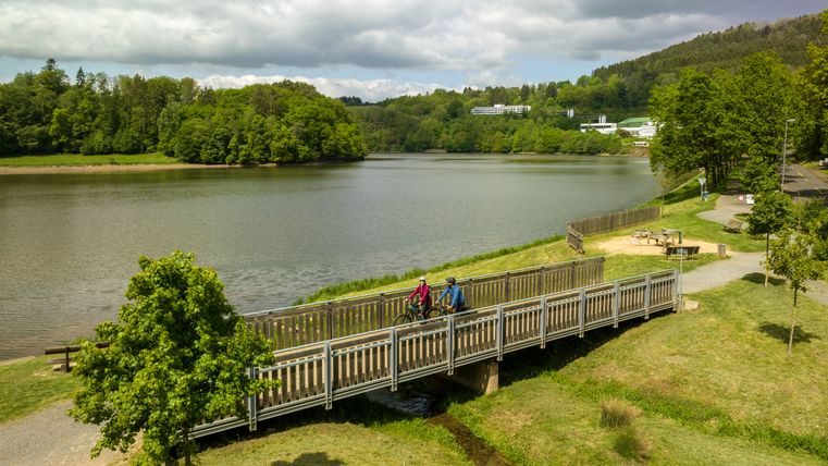 Two cyclists on a bridge over a tributary in front of the reservoir