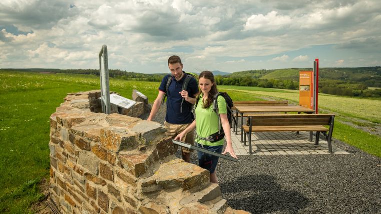 Twee wandelaars bekijken een informatiebord bij een Romeinse villa-ruïne op een wandelroute.
