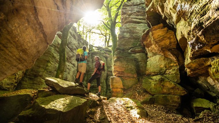 Two hikers in a rocky gorge with sunlight and trees.