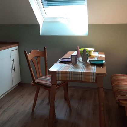 Une cuisine cosy avec un petit coin repas. La table est dressée et la lumière tombe à travers une fenêtre sur les meubles.