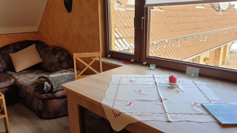 Een gezellige kamer met een bank en een tafel. Door het raam is er uitzicht op het dak van een aangrenzend gebouw.