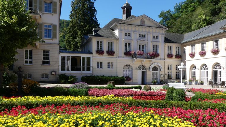 Ein hübsches Gebäude umgeben von bunten Blumenbeeten. Die Szene strahlt eine ruhige und einladende Atmosphäre aus.