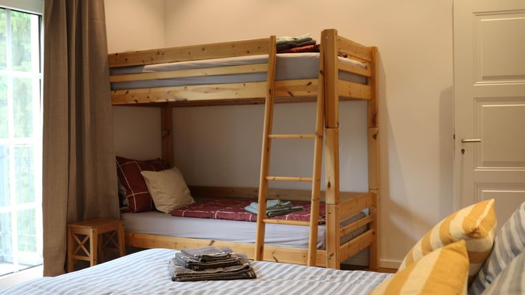 Ein gemütliches Schlafzimmer mit einem Etagenbett aus Holz und einem großen Doppelbett. Das Zimmer hat große Fenster und eine einladende Atmosphäre.