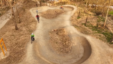 Een BMX-trace met meerdere bochten en sprongen. Fietsers genieten van de baan in een schaduwrijke omgeving.