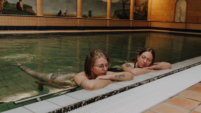 Twee vrouwen ontspannen aan de rand van het zwembad. Het water is kalm en de sfeer is vredig.