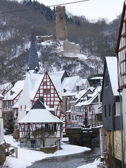 Een schilderachtig dorp in de sneeuw met vakwerkhuizen en een kleine rivier. Op de achtergrond staat een oude toren op een heuvel.