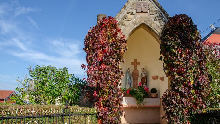 Een kleine kapel met beelden en rode klimplanten in Wolsfeld.
