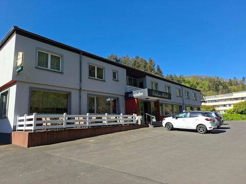 A small inn with a bright facade and an inviting entrance area. Several cars are parked in front of the building.