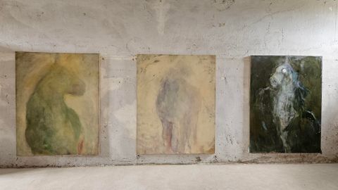 Three abstract paintings hang on a wall in an empty room. The colors are soft and the shapes are vaguely recognizable.