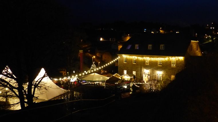 A festively lit Christmas market at dusk. Stalls and a tent are beautifully decorated, while the atmosphere feels cozy.