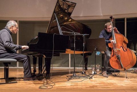 Two musicians are playing live on a stage. The pianist is sitting at the piano and the double bassist is standing next to him.