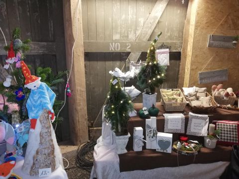 Een kerstmarktkraam met kleine decoratieve boompjes en verschillende cadeaus. De sfeer is gezellig en feestelijk.