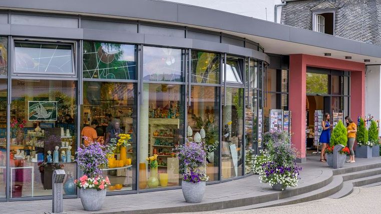 Un magasin moderne avec de grandes fenêtres en verre et des fleurs colorées sur la terrasse. Des gens entrent dans le magasin et profitent de la variété des produits proposés.
