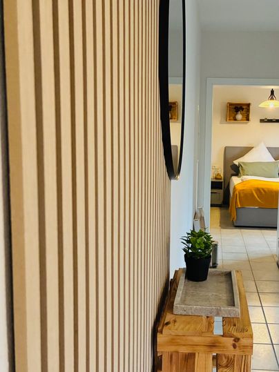 De ruimte toont een elegante wand met verticale houtplanken en een ronde spiegel. Een houten tafel met een klein plantje staat op de voorgrond.