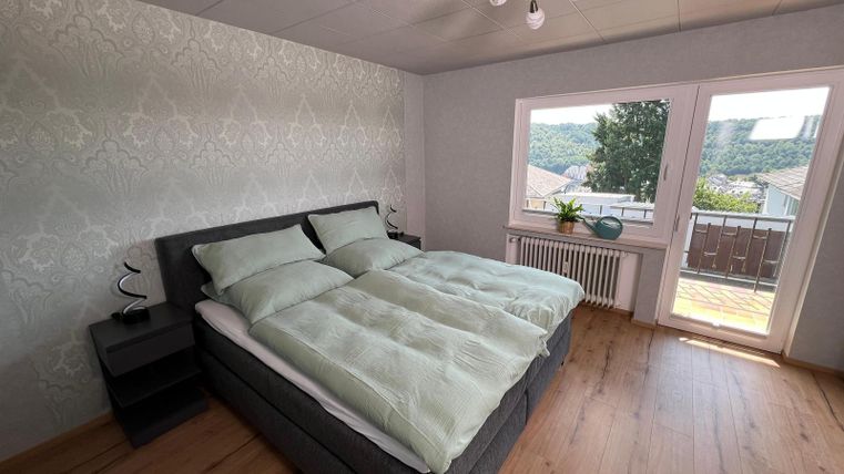 A modern bedroom with a large double bed and bright bedding. The room has a beautiful view of nature through large windows.