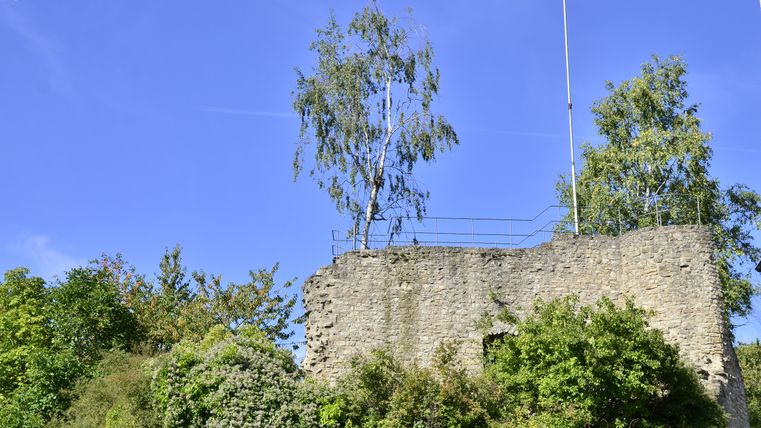 Viewing platform on the ruins of Bettingen Castle in the Southern Eifel Nature Park, surrounded by trees and blue skies.
