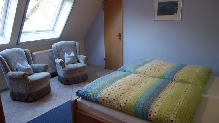 A cozy bedroom with a large bed and two armchairs. The walls are painted blue and there is a window with natural light.