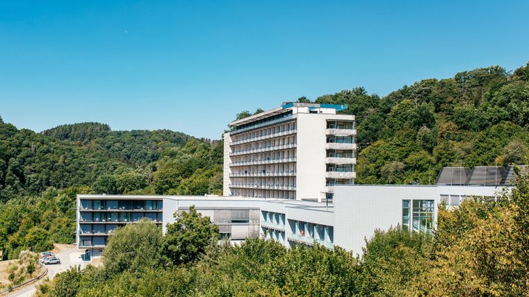 Ein modernes Hotel umgeben von grünen Bäumen und Hügeln. Der klare Himmel bietet eine angenehme Atmosphäre.
