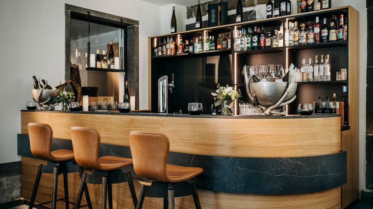 Un bar élégant avec des éléments en bois et en pierre. Sur l'étagère, diverses spiritueux et boissons sont visibles.