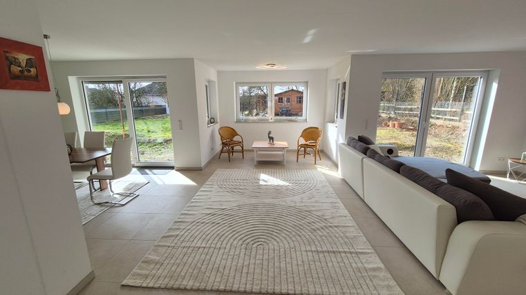 Une pièce à vivre lumineuse et moderne avec de grandes fenêtres et un canapé confortable. La pièce est décorée d'un tapis et de meubles simples.